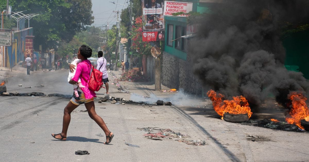 Une femme, un enfant dans les bras, court se mettre à l'abri pendant des tirs des bandes armées, le 20 mars 2024 à Port-au-Prince, en Haïti