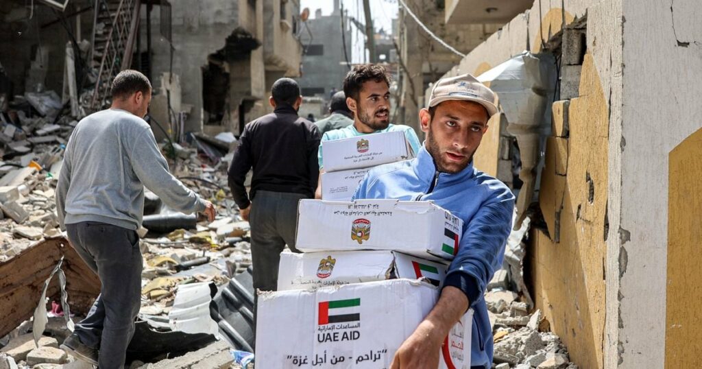 Des hommes marchent au milieu des décombres de bâtiments en portant des colis d'aide humanitaire largués au-dessus du nord de la bande de Gaza, le 23 avril 2024