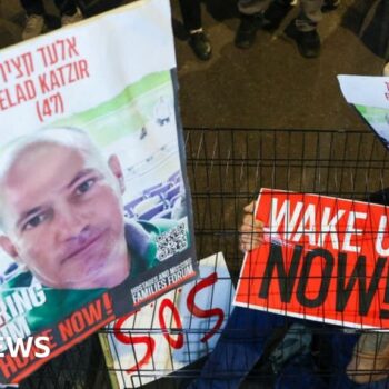 A man sits in a cage with portraits of hostage Elad Katzir during a demonstration in Tel Aviv in March