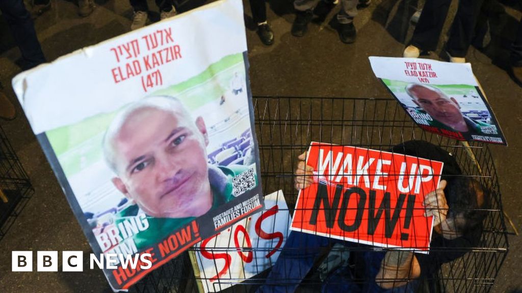 A man sits in a cage with portraits of hostage Elad Katzir during a demonstration in Tel Aviv in March