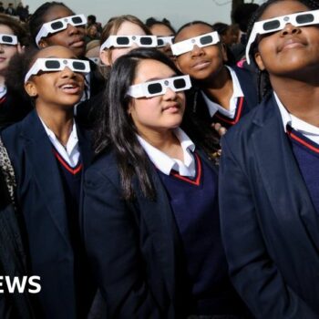 School children look at a solar eclipse through dark glasses