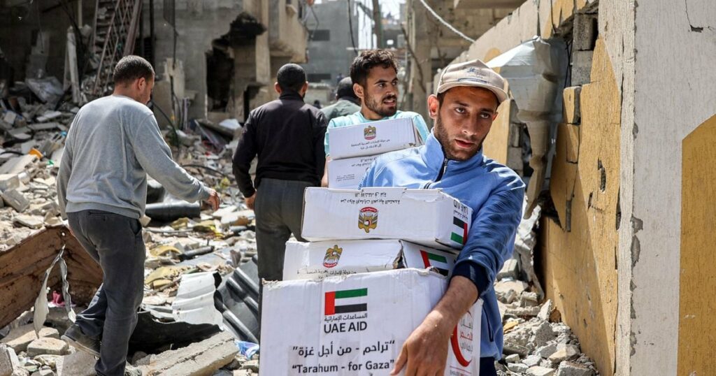 Des hommes marchent au milieu des décombres de bâtiments en portant des colis d'aide humanitaire largués au-dessus du nord de la bande de Gaza, le 23 avril 2024