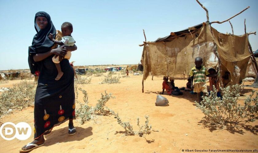 A Sudanese woman fills water bottles held by a young boy