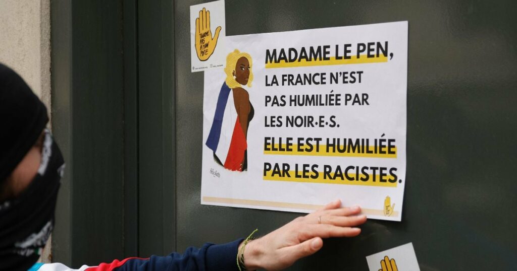 Un manifestant colle une affiche clamant "Madame Le Pen, la France n'est pas humiliée par les noirs, elle est humiliée par les racistes" sur le siège du Rassemblement national lors d'une manifestation de SOS Racisme en soutien à la chanteuse Aya Nakamura, à Paris, le 24 mars 2024