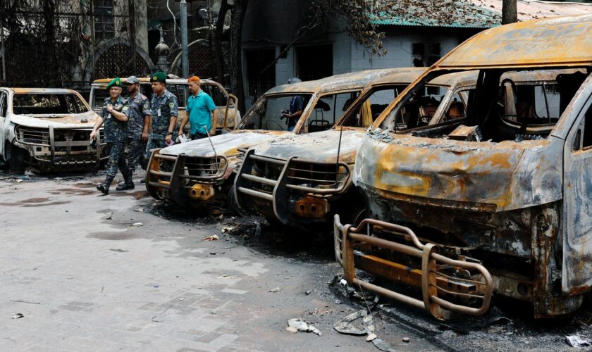 Security personnel walk past damaged vehicles of a government owned organization in Dhaka