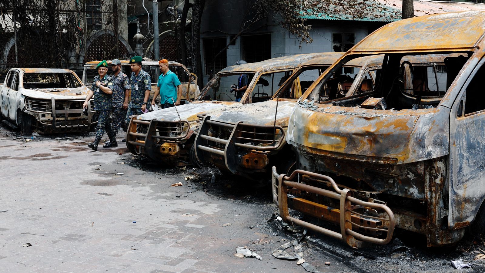 Security personnel walk past damaged vehicles of a government owned organization in Dhaka