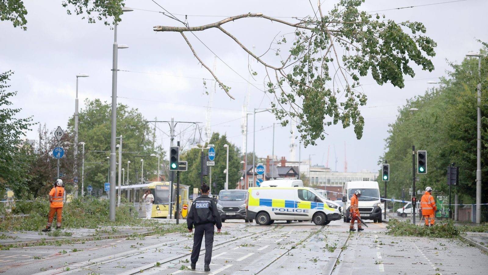 A police officer looks on as workers begin to remove fallen tree branches after strong winds brought by Storm Lilian brought down trees blocking roads and tram routes in Manchester, Britain, August 23, 2024. REUTERS/Phil Noble