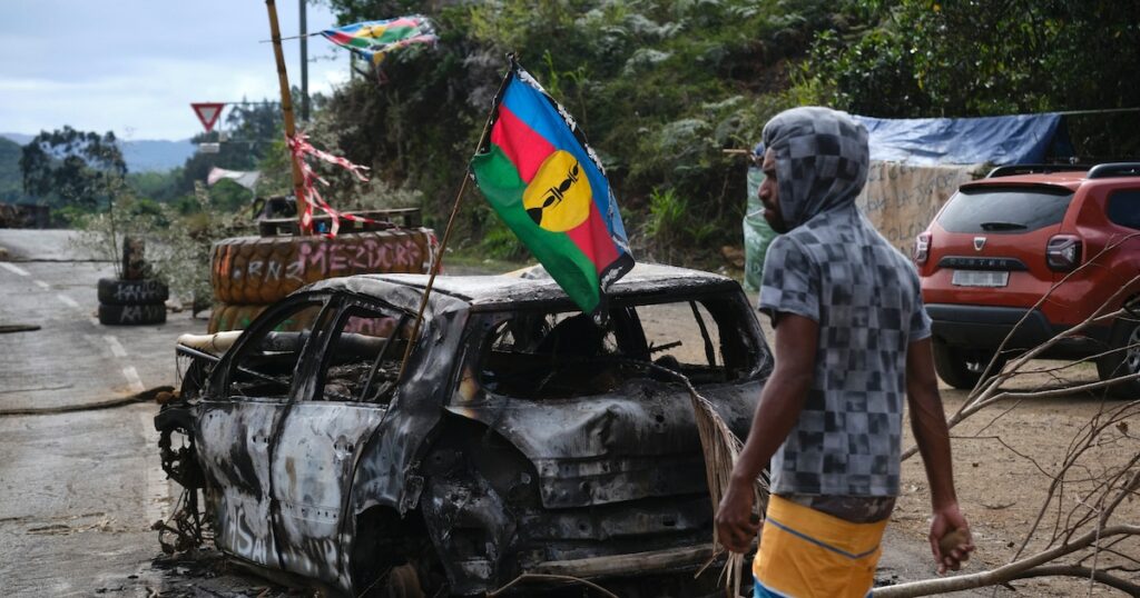 Un manifestant indépendantiste kanak près d'un véhicule calciné portant un drapeau du FLNKS lors d'un barrage routier à Houaïlou, sur la côte est de la Nouvelle-Calédonie, le 1er juillet 2024