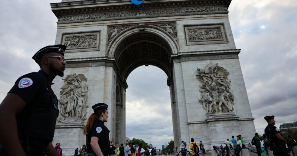 Des policiers passent devant l'Arc de triomphe arborant le sigle des Jeux paralympiques de Paris, le 22 juillet 2024