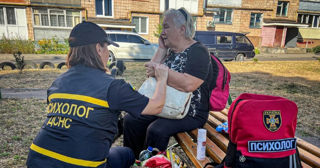 Photo diffusée par les services d'urgence ukrainiens, le 26 août 2024, d'une psychologue réconfortant une femme âgée après une frappe de missile russe à Loutsk, dans la région de Volhynie, en Ukraine