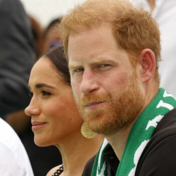 Prince Harry looking serious, sat next to Meghan Markle