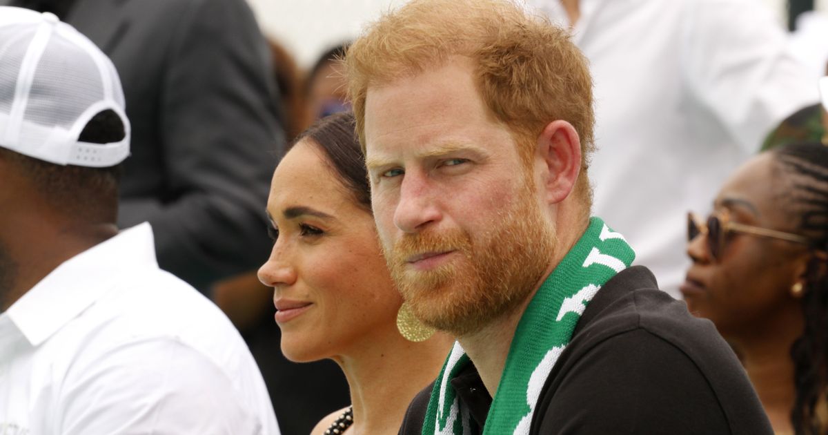 Prince Harry looking serious, sat next to Meghan Markle