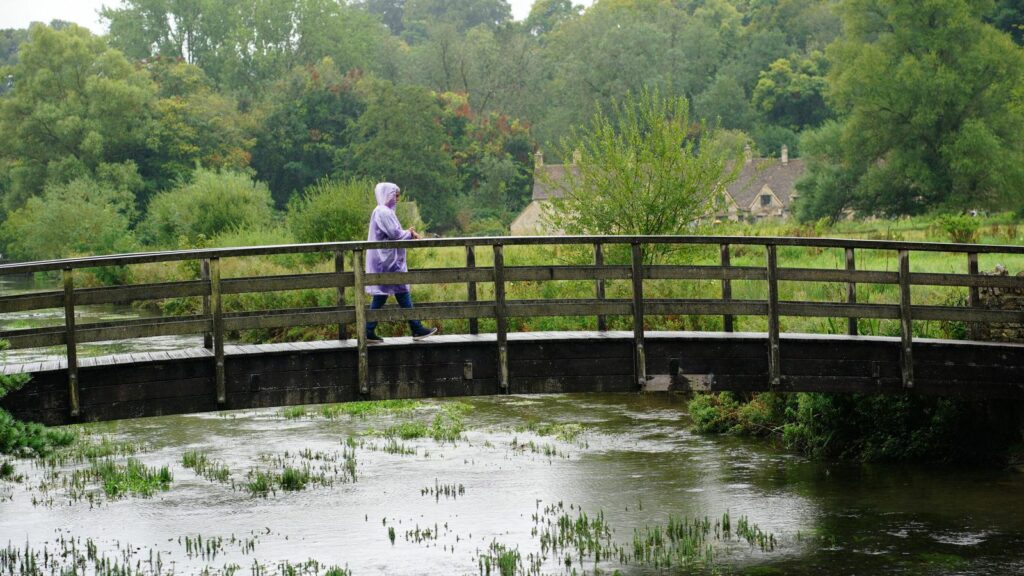 A visitor to Bibury village in Gloucestershire braves the rainy weather. Pic: PA