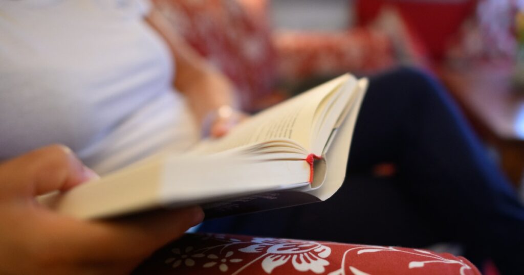 Une femme lit un livre sur un canapé.