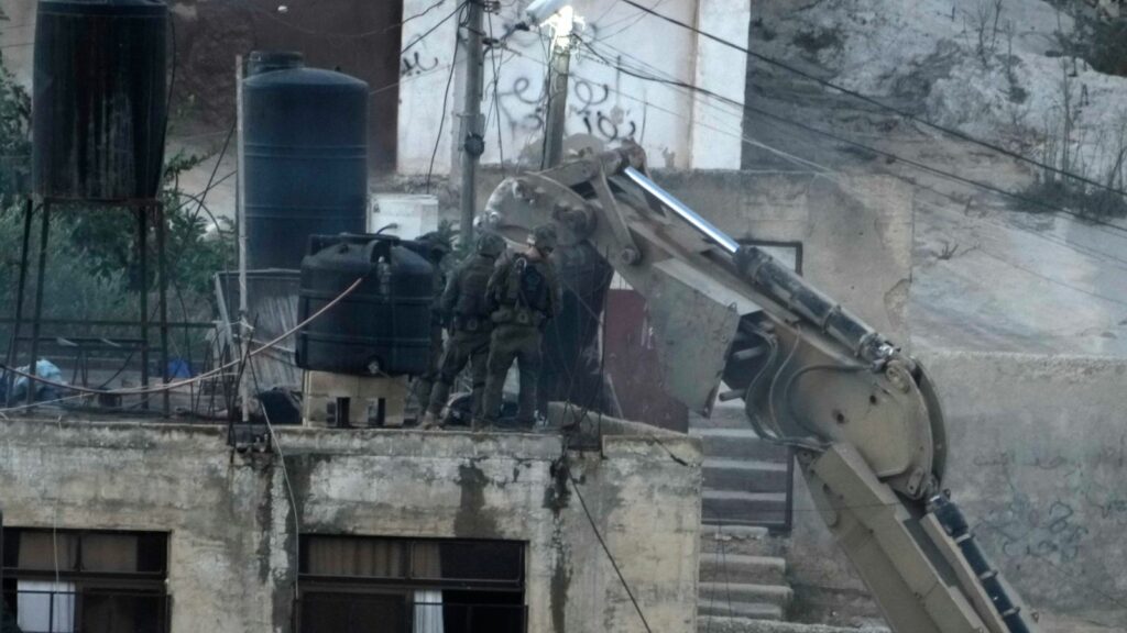 Israeli soldiers look over a rooftop where two bodies lie motionless in the West Bank town of Qabatiya. Pic: AP