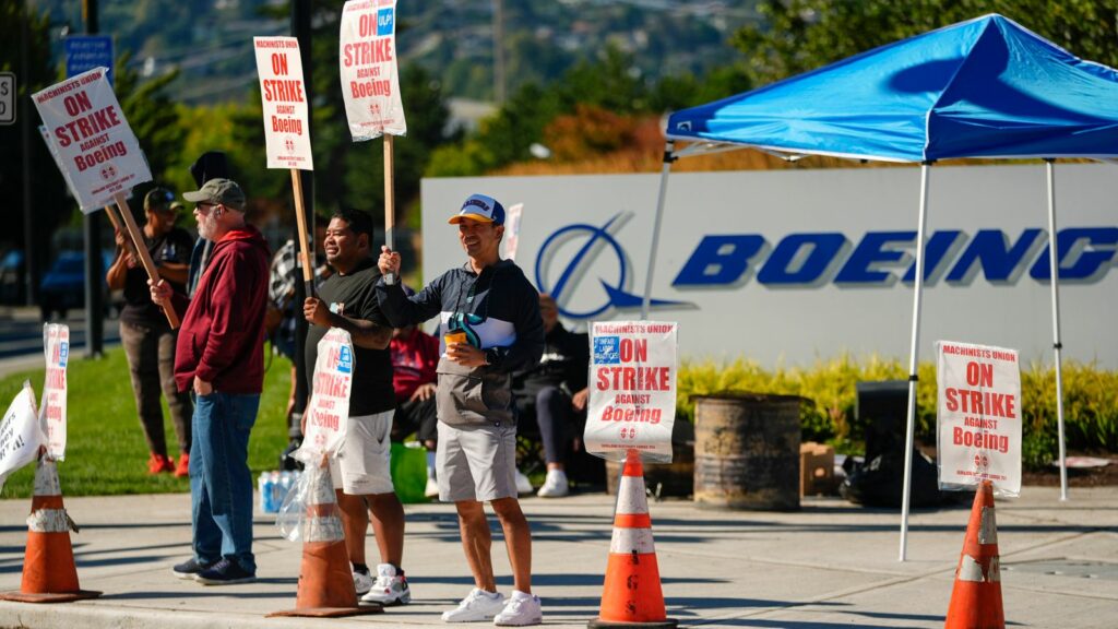 Boeing employees Cham Sin, in black, and Lou Saephanh, right center, wave signs as Boeing workers continue to strike Tuesday, Sept. 24, 2024, near the company's factory in Renton, Wash. (AP Photo/Lindsey Wasson)