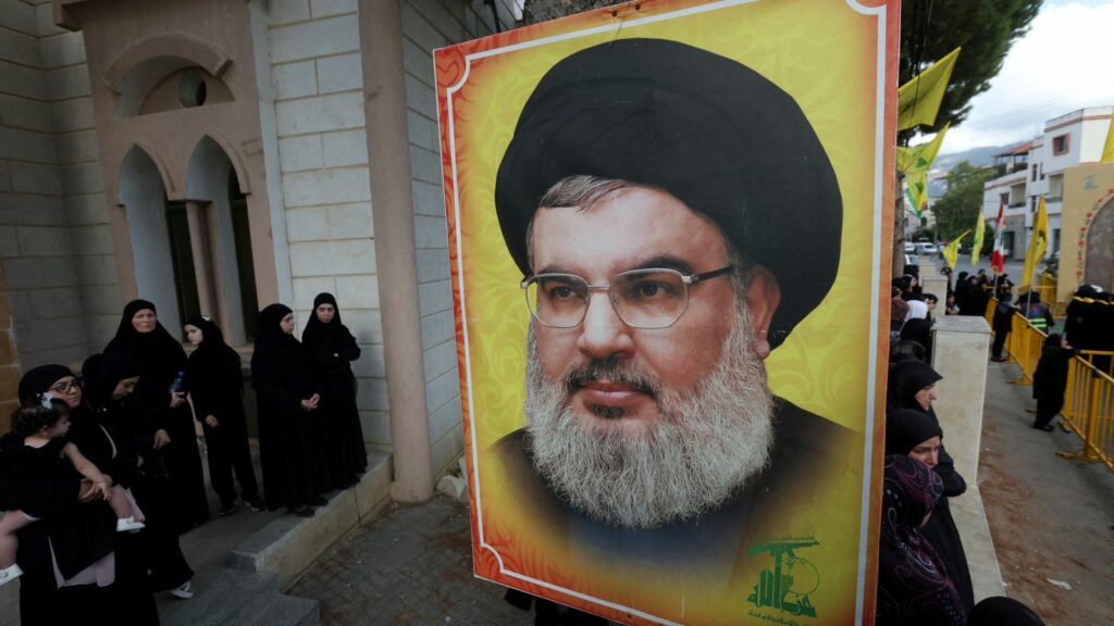 People stand near a picture of Hezbollah leader Sayyed Hassan Nasrallah during the funeral of Hezbollah member Ali Mohamed Chalbi, after hand-held radios and pagers used by Hezbollah detonated across Lebanon, in Kfar Melki, Lebanon September 19, 2024. REUTERS/Aziz Taher