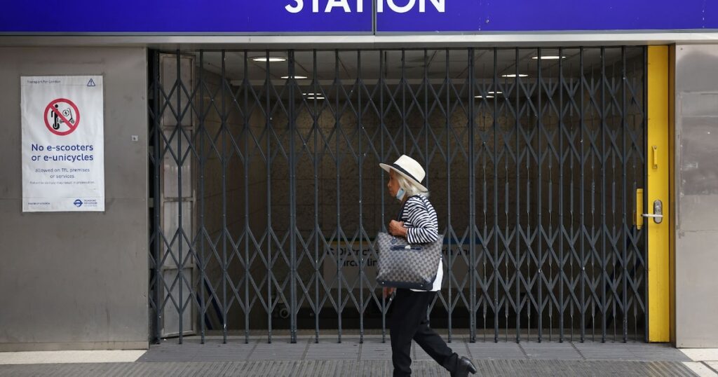 Une passante marche devant les grilles fermées de la station de métro Victoria à Londres le 19 août 2022, alors que le réseau de transports en commun de la capitale britannique est très perturbé par une grève pour les salaires face à l'inflation