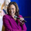 Kamala Harris sitzt auf einer Bühne und lacht, während sie mit links ein Mikro hält