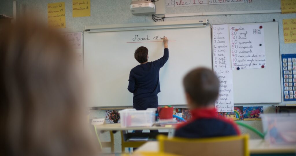 A teacher wearing a protective face mask works with pupils after they have returned to their classroom at the Trinite public school in the Groix island, on May 12, 2020, two days after France eased lockdown measures to curb the spread of the COVID-19 pandemic, caused by the novel coronavirus. (Photo by Loic VENANCE / AFP)