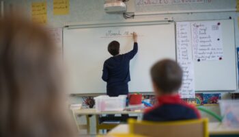 A teacher wearing a protective face mask works with pupils after they have returned to their classroom at the Trinite public school in the Groix island, on May 12, 2020, two days after France eased lockdown measures to curb the spread of the COVID-19 pandemic, caused by the novel coronavirus. (Photo by Loic VENANCE / AFP)