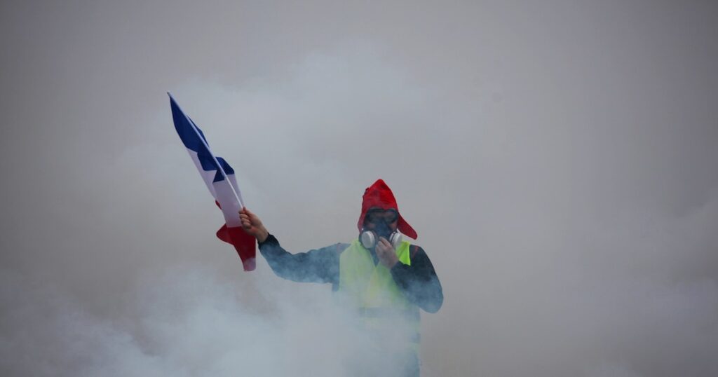 Un "gilet jaune" tient le drapeau français dans la fumée des gaz lacrymogènes lors d'une manifestation contre la hausse du coût de la vie, le 1er décembre 2018 à Paris