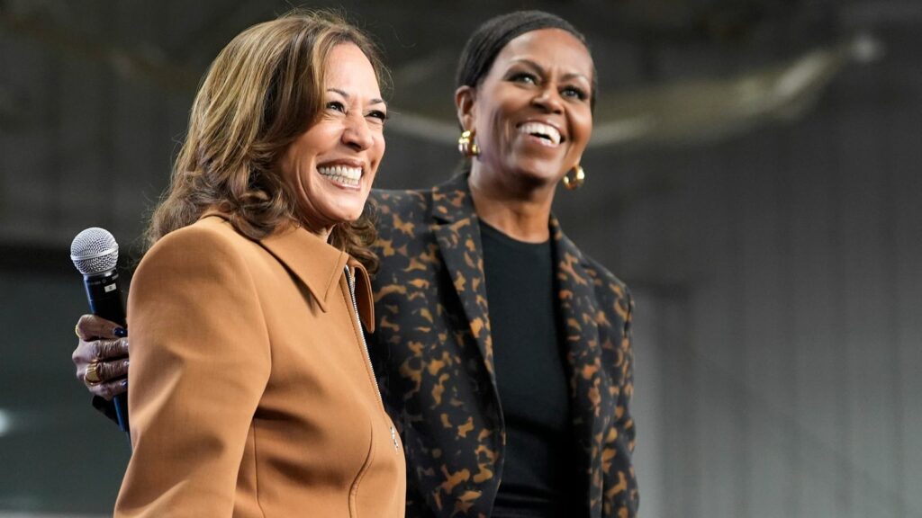 Former first lady Michelle Obama, right, and Democratic presidential nominee Vice President Kamala Harris address the crowd in the overflow space of a campaign rally at the Wings Event Center in Kalamazoo, Mich. (AP Photo/Jacquelyn Martin)