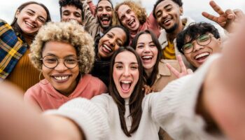 Eine Frau lacht mit vielen Freundin auf einem Selfie.