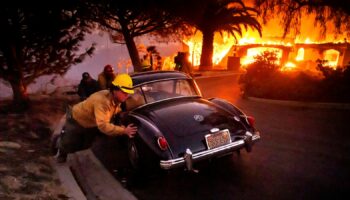 Firefighters and sheriff's deputies push a vintage car away from a burning home as the Mountain Fire burns in Camarillo, Calif., on Wednesday, Nov. 6, 2024. (AP Photo/Noah Berger)