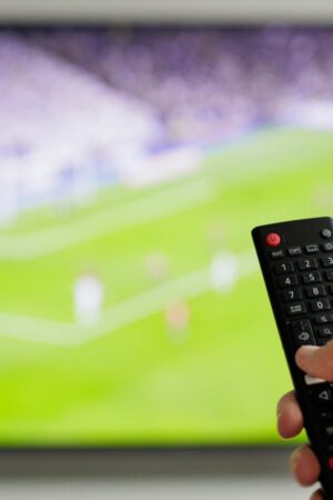 Close up of hand with remote controller and tv with football on background