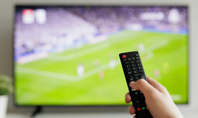 Close up of hand with remote controller and tv with football on background