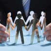 Businessman's Hands Protecting Team Of Paper People On Desk