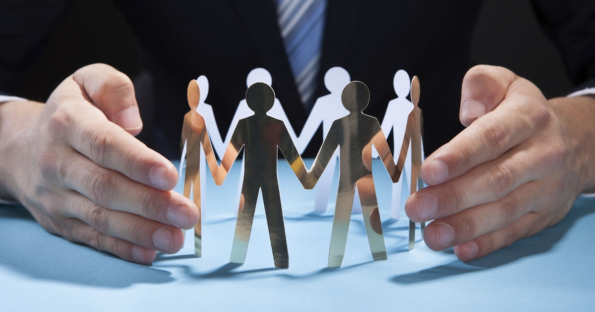 Businessman's Hands Protecting Team Of Paper People On Desk