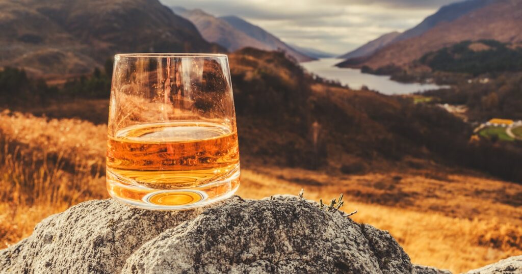 Glass of single malt Scotch Whisky on an old rock above Glenfinnan in the West Highlands of Scotland.