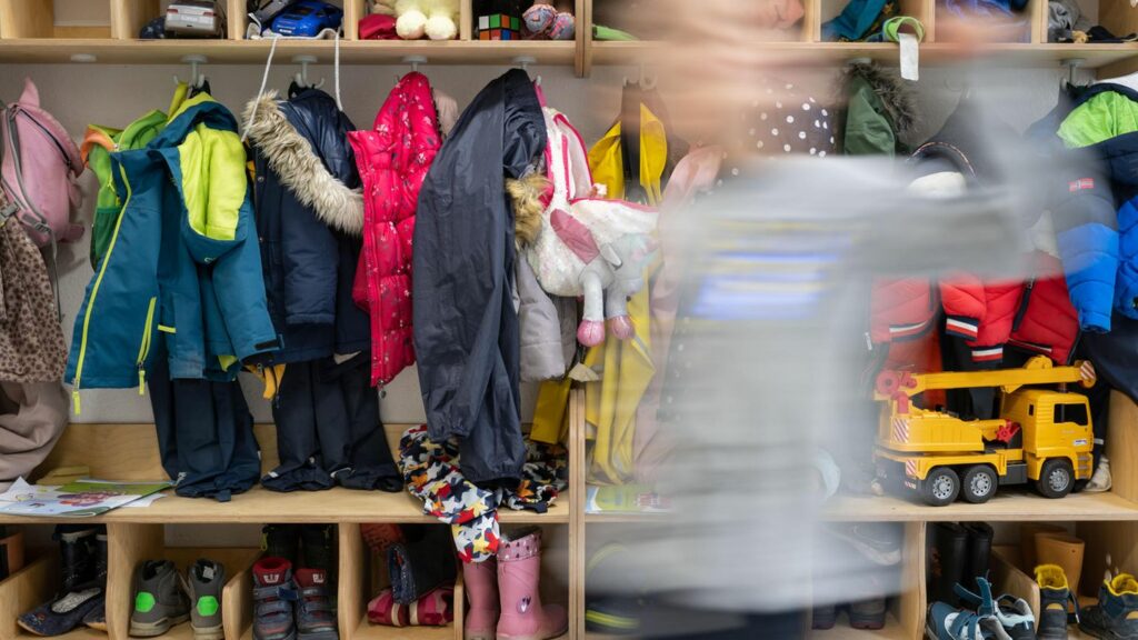 Ein Kind einer Kindergartengruppe läuft an der vollen Garderobe vorbei