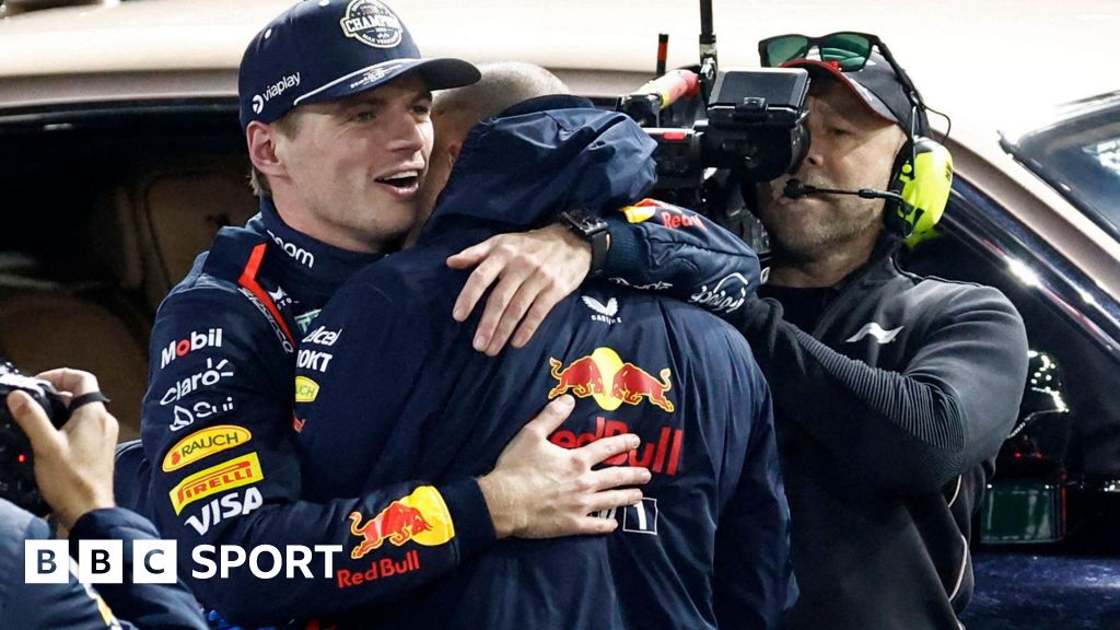 Max Verstappen embraces a Red Bull team member after winning the F1 world title, with a TV cameraman in the background