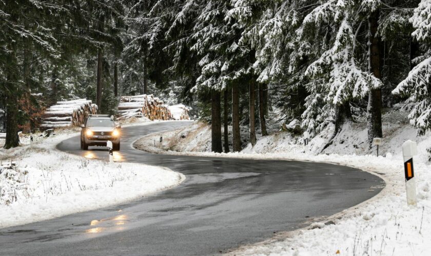 Ein Auto fährt auf einer nassen Straße durch einen Wald voller Schnee