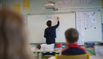 A teacher wearing a protective face mask works with pupils after they have returned to their classroom at the Trinite public school in the Groix island, on May 12, 2020, two days after France eased lockdown measures to curb the spread of the COVID-19 pandemic, caused by the novel coronavirus. (Photo by Loic VENANCE / AFP)