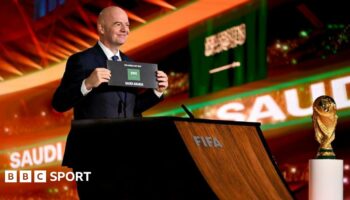 Gianni Infantino holds up a card and stands next to the World Cup trophy