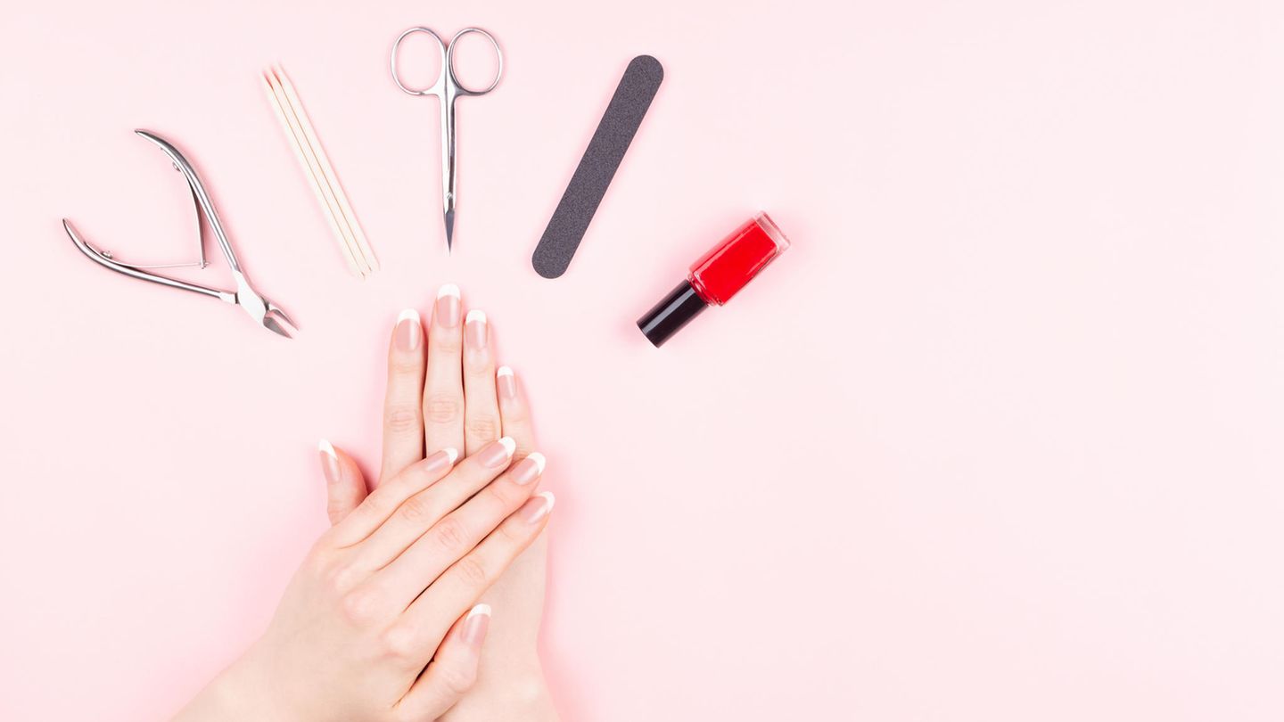 Nagelfeile Handgepäck: Gepflegte Hände und ein Manikür-Set liegen auf einem rosa Tisch.