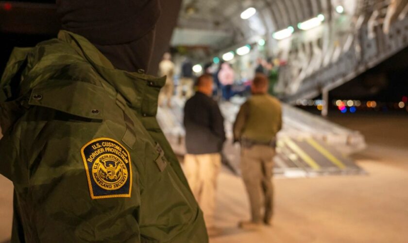 This photo provided by the U.S. Dept. of Defense, A U.S. Customs and Border Protection agent watches as undocumented immigrants are loaded onto a C-17 Globemaster III at Tucson International Airport in Tucson, Ariz., Thursday, Jan. 23, 2025.  (Senior Airman Devlin Bishop/Dept. of Defense via AP)