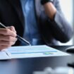 Millennial businessman wearing formal wear working with statistical document in modern office.