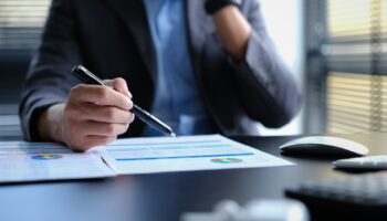 Millennial businessman wearing formal wear working with statistical document in modern office.