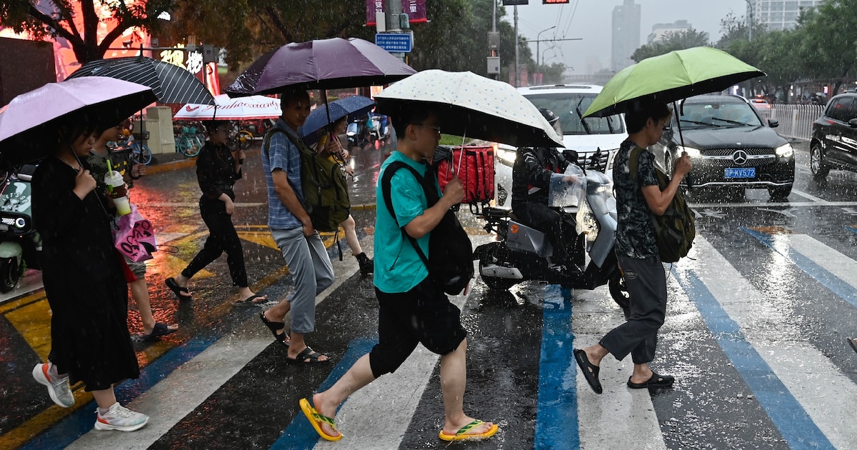 Des passants s'abritent sous des parapluies durant un orage, à Pékin le 30 juillet 2024.