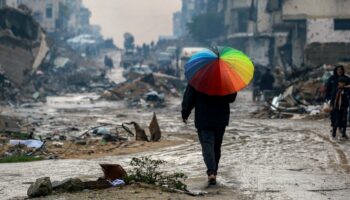 Un homme marche avec un parapluie aux couleurs de l'arc-en-ciel sur une rue boueuse au milieu des décombres dans le nord de Gaza, le 10 février 2025