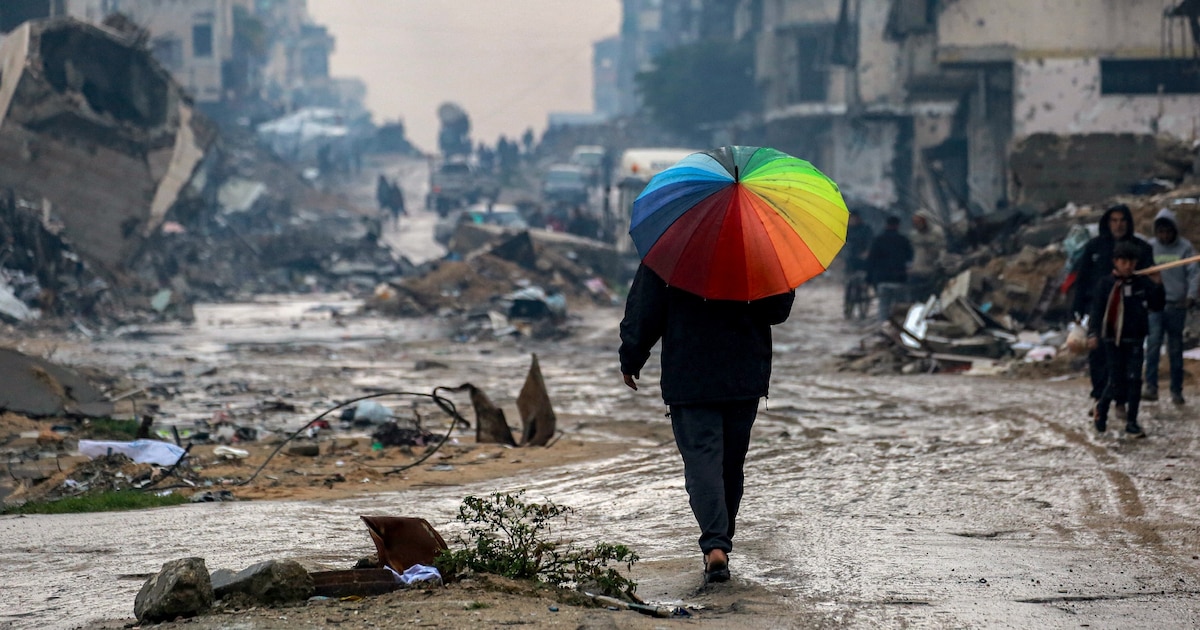 Un homme marche avec un parapluie aux couleurs de l'arc-en-ciel sur une rue boueuse au milieu des décombres dans le nord de Gaza, le 10 février 2025